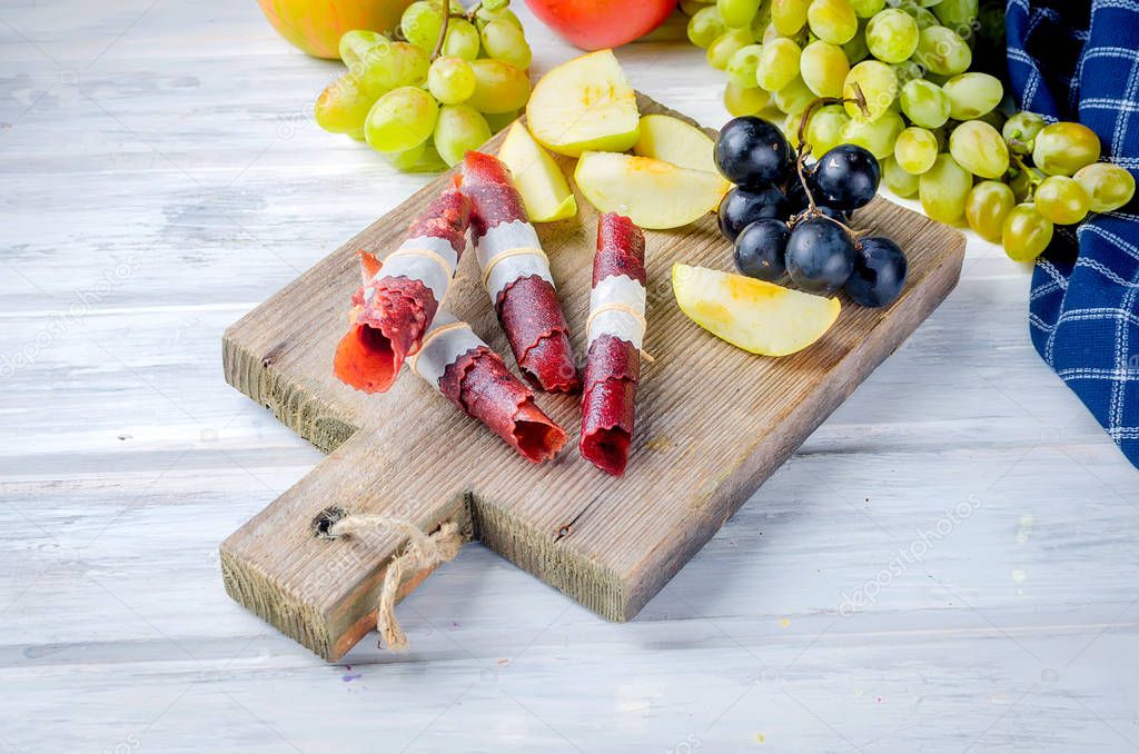 Fresh yellow apples, white and blue grapes, scattered on the  table, slice fruits and fruit leather rolls on white wooden table. Detox concept. Healthy food, Fruits amazing candy. selective focus, Copy Space 