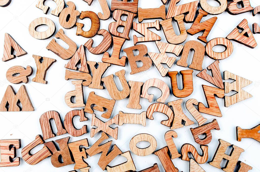 scattered mixed brown wooden letters of the English alphabet on white background, copy space, as a background composition 