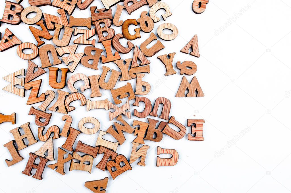 scattered mixed brown wooden letters of the English alphabet on white background, copy space, as a background composition 