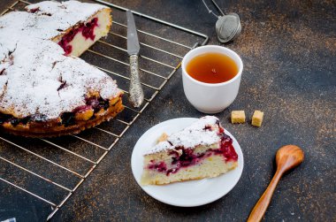 Kiraz veya erik Pasta krema şeker, rustik koyu arka plan üzerinde çay ile serpilir yakın çekim, yukarıdan görünüm 