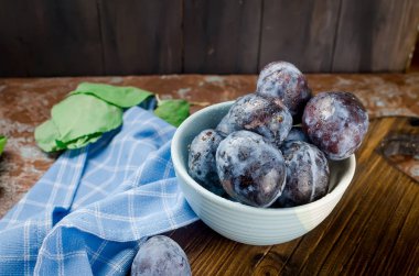 Bir seramik kase ve koyu kahverengi rustik arka plan seçici odak, kopya alanı yapraklarda mavi Erik 
