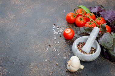 Bir taş harç ve bir sürü yeşil ve kırmızı fesleğen ve olgun domates, sarımsak, baharatlar tuz karanlık bir taş arka plan üzerinde. Üstten görünüm, kopya alanı.