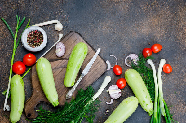 Young spring zucchini, tomatoes, herb and spices on black background from above. Fresh spring vegetables for frying. Background layout with free text space. Top view. copy space.