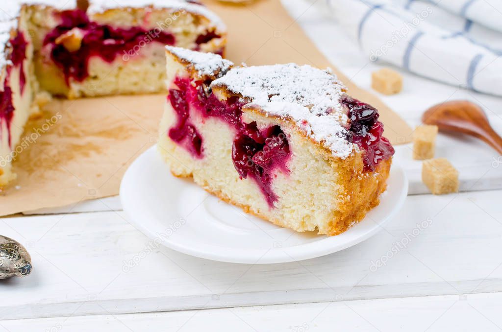 Cherry or plum pie sprinkled with icing sugar, cup of tea  on white wooden boards, close-up, view from above 
