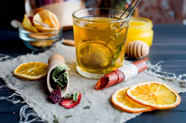 Cup of green tea  with mint,  lemon slice, dry fruits roll and tea mint leaves with strawberry in a wooden spoon on wooden background, copy space