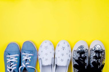 üç farklı çift ayakkabı bir genç kız, tuval, slipons, spor ayakkabıları, sarı zemin üzerine şık ayakkabılar için. Güzellik ve moda kavramı. Düz yatıyordu, en iyi görünümü kopya alanı. 