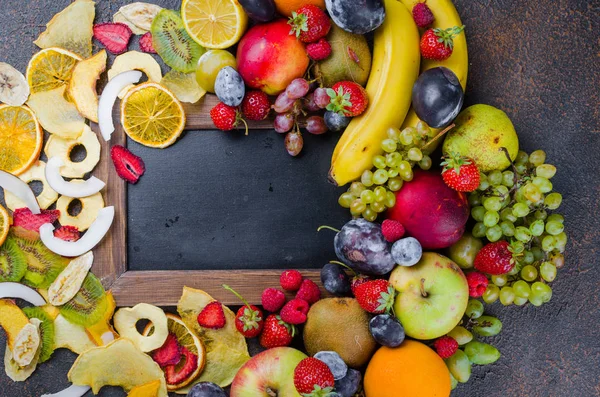 Raw ripe fruits and Fruit chips laid out around with an empty space for text on dark background , concept of healthy and proper nutrition, snack, top view, copy space