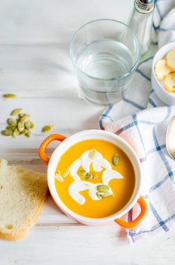 Tohumlar, ekşi krema ve ekmek kruton beyaz rustik ahşap zemin üzerinde seramik kase ev yapımı balkabağı çorbası 