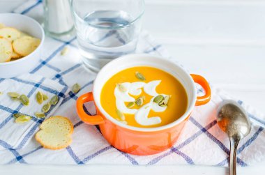 Tohumlar, ekşi krema ve ekmek kruton beyaz rustik ahşap zemin üzerinde seramik kase ev yapımı balkabağı çorbası 