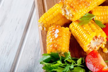 Lezzetli ızgara mısır koçanı Solta, bitki, baharat, tereyağı ve beyaz ahşap masa, domates ile yakın çekim 