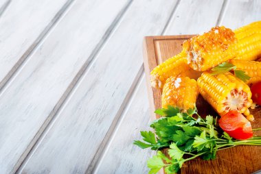 Lezzetli ızgara mısır koçanı Solta, bitki, baharat, tereyağı ve beyaz ahşap masa, domates ile yakın çekim 