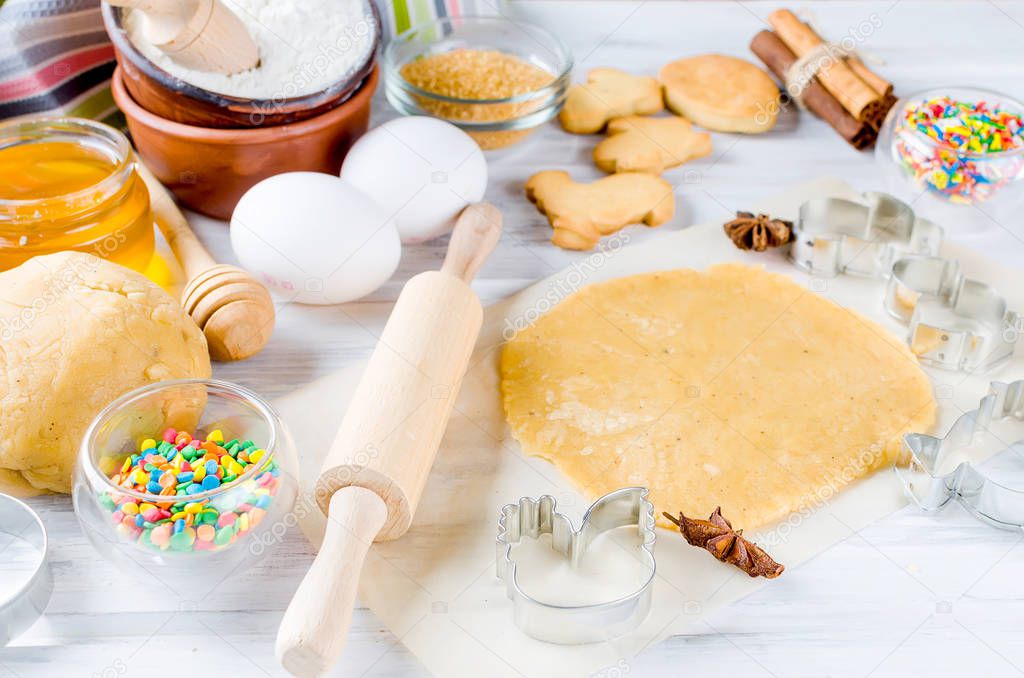 Easter cooking background, dough and indredients, cuts for cookies and colored sugar decor for baking on a white background, The process of making fragrant Easter cookies, series photo, top view, flat lay, copy space