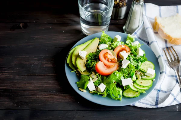 Taze yeşil salata salatalık, marul, avokado ve domates ve koyu ahşap bir masa cam su ile. Gıda sağlıklı yaşam konsepti. Düz yatıyordu. Metin, doğal ışık, seçici focu için yer kopyalayın