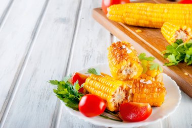 Lezzetli ızgara mısır koçanı Solta, bitki, baharat, tereyağı ve beyaz ahşap masa, domates ile plaka üzerinde Kapat 