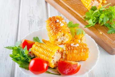 Lezzetli ızgara mısır koçanı Solta, bitki, baharat, tereyağı ve beyaz ahşap masa, domates ile plaka üzerinde Kapat 