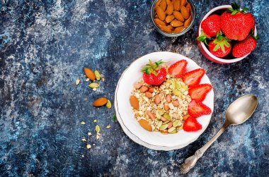 Taze ev yapımı granola, çilek, badem, fıstık ve tohum bir koyu gri arka plan, seçici odak, üstten görünüm, beyaz bir plaka ile müsli alanı Kopyala