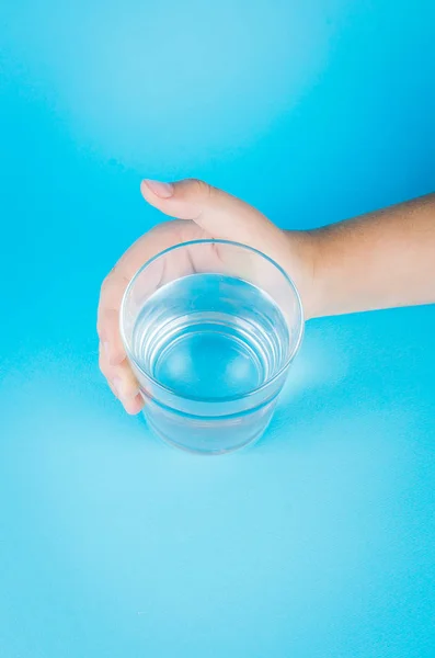 Glass of water in hand on blue — Stock Photo, Image