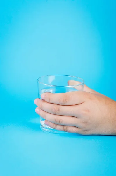 Стакан воды в руке на голубом — стоковое фото