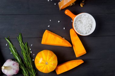 Kesme tahtasındaki çiğ balkabağı parçaları biberiye, tuz, baharat ve eski karanlık masa. Fırında pişirmek için sebze hazır. Sonbahar ev yemekleri