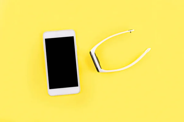Трэкер с белым браслетом и телефоном на желтом фоне — стоковое фото