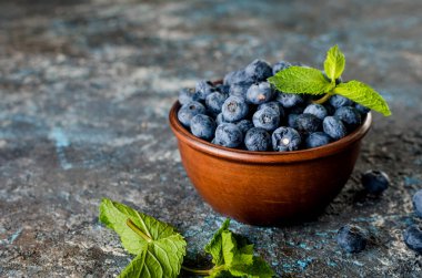 Seramik kasede olgun yaban mersinleri ve koyu beton arka planda nane yaprakları.
