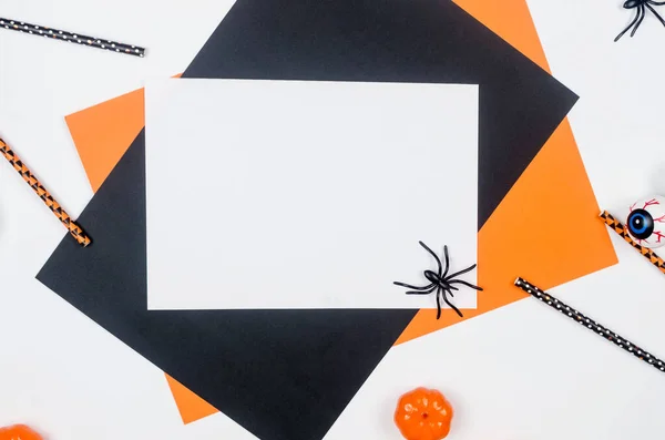 Halloween party composition on paper background in black, orange and white. Flat lay, Halloween party decor - drink straws, pumpkins, bats and spiders. Mock-up, greeting card, flat lay, top view.