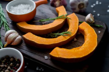 Kesme tahtasındaki çiğ balkabağı parçaları biberiye, tuz, baharat ve eski karanlık masa. Fırında pişirmek için sebze hazır. Sonbahar ev yemekleri.