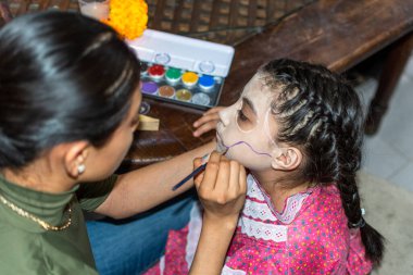 Anne, festival için kızının yüzüne Catrina makyajı yapıyor.