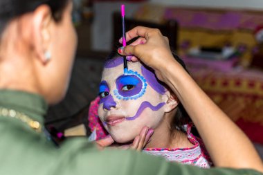 Anne, festival için kızının yüzüne Catrina makyajı yapıyor.