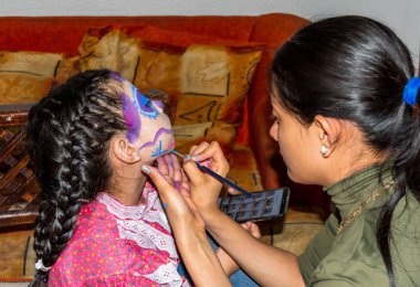 Anne, festival için kızının yüzüne Catrina makyajı yapıyor.