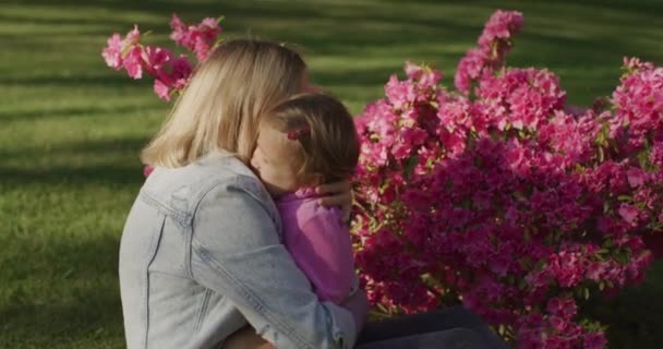 Mujer bastante joven con su pequeña niña divirtiéndose con flores en el parque — Vídeos de Stock