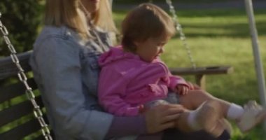 Küçük kızı salıncakta sallanan genç bir kadın. Parkta küçük kızıyla güzel bir anne.