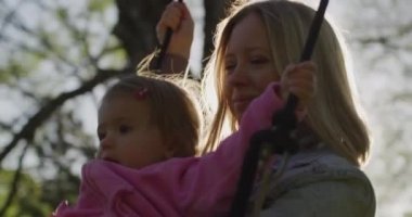 Küçük kızı salıncakta sallanan genç bir kadın. Parkta küçük kızıyla güzel bir anne.