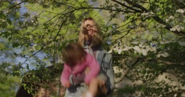 Όμορφη γυναίκα κρατά το κοριτσάκι της στην αγκαλιά της στο καλοκαιρινό πάρκο. — Αρχείο Βίντεο
