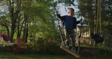 Yeşil bir parkta salıncakta sallanan küçük bir çocuk. Mutlu çocukluk.