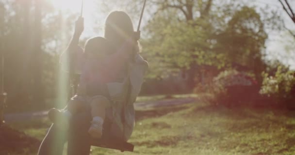 Mujer joven con su bebé en un columpio. bastante joven mamá con su bebé niña en parque — Vídeos de Stock