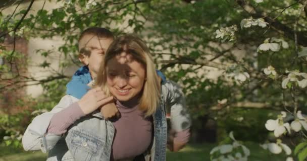 Ładna młoda kobieta bawiąca się ze swoim synkiem. Mały chłopiec na plecach mamy. — Wideo stockowe