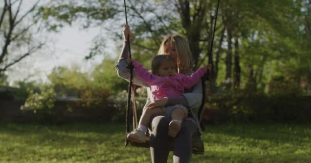 Młoda kobieta z córeczką na huśtawce. ładna młoda mama z jej dziewczynka w parku — Wideo stockowe