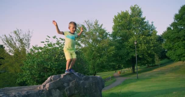 Netter kleiner Junge, der im Sommerpark vom Felsen springt. Rote Kinokamera. Zeitlupe 4k — Stockvideo