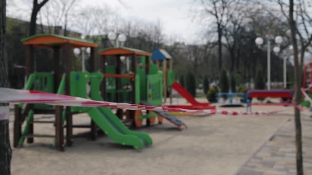 Röd och vit randig barrikadtejp, ofokuserad stängd tom färgglad lekplats utomhus. Lekplats för barn spärras av på grund av karantän och COVID-19 förlängning förebyggande. Avslutande av — Stockvideo
