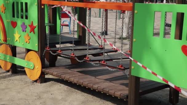 Stängt tom färgglad lekplats utomhus. Lekcenter för barn spärrade av med röd och vit randig barrikadtejp på grund av karantän och COVID-19 förlängning förebyggande. Avslutande av barndomen — Stockvideo