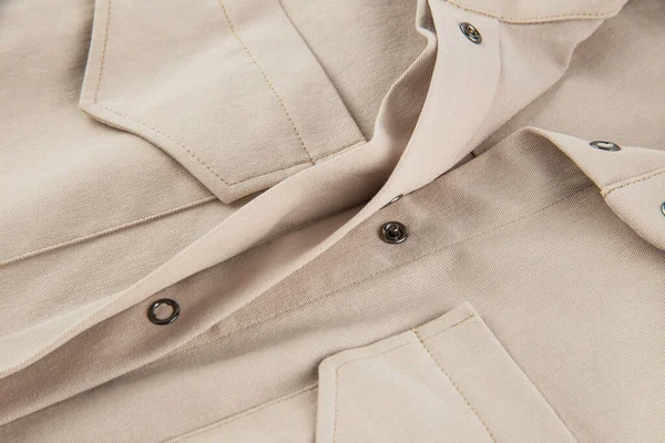 a fragment of a patch pocket with a flap and a button closure on a beige shirt made of thick cotton fabric