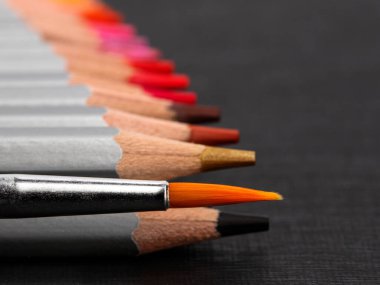 Gümüş gömlekli, sivri renkli kalemler ve siyah bir arka planda bir sanat fırçası.