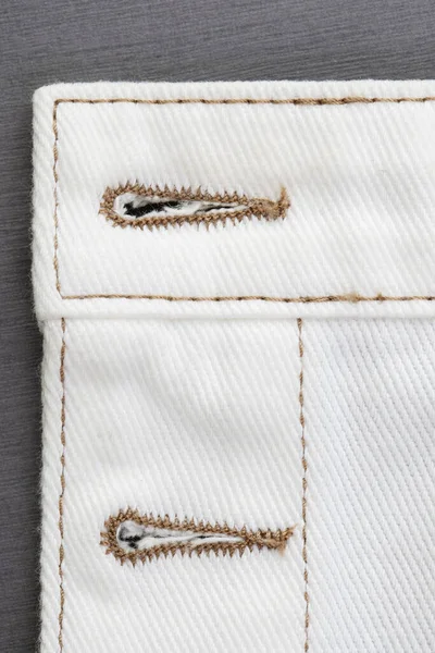 white denim fabric, connecting parts with various seams with brown threads, raw edge with fringe
