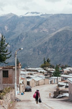 PINCHOLLLO, COLCA VALLEY, PERU - 20 HAZİRAN 2018: Perulu bir kız dağlı bir çantayla caddeyi geçiyor. Pinchollo, Colca Valley, Peru 'daki küçük bir köyde.