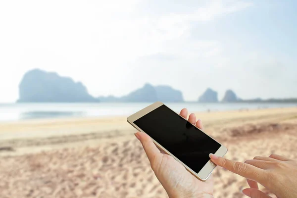 Hand using smart phone with blur photo of the beach — Stock Photo, Image