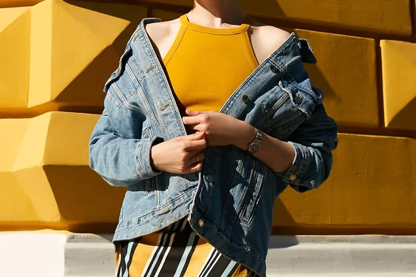 Fashionable denim jacket dropped from the shoulders of a woman in a yellow top. Street style.