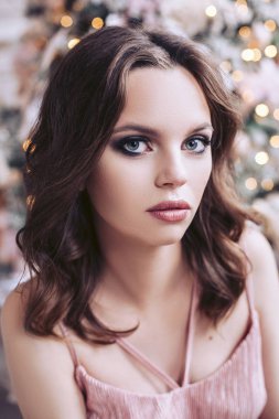 Arka planda çelenk süslenmiş Noel ağacı ile bir pembe elbiseli bir kız portresi.