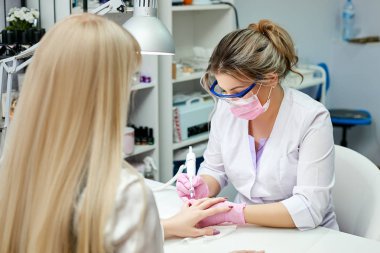 Laboratuar önlüğünü çivi yöneticisinde donanım manikür güzellik salonu içinde yapar. Temizleme jeli vernik freze kesici ile. Beyaz masa.