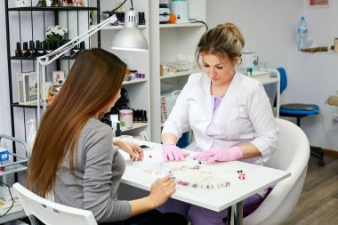 Beyaz bir elbise içinde manikür ana esmer kız bir salonda renkli çivi'nin yardımcı olur